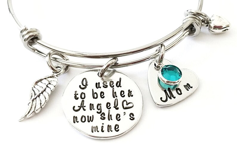 May include: Silver bangle bracelet with a charm that reads "I used to be her Angel now she's mine" and a heart charm with a turquoise stone that reads "Mom".