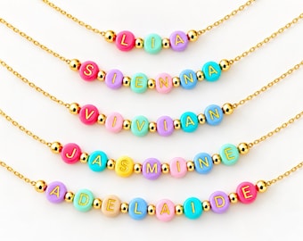 Puede incluir: Cinco collares de cadena dorada con cuentas redondas de colores y letras doradas que forman los nombres LIA, SIENNA, VIVIAN, JASMINE y ADELAIDE. Cada collar está decorado con pequeñas cuentas espaciadoras doradas entre las letras.