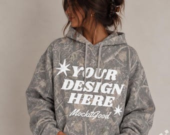 May include: A grey and brown camouflage print hooded sweatshirt featuring a front kangaroo pocket and long sleeves. The text "YOUR DESIGN HERE" is printed in large white letters on the chest, accompanied by two white star icons and the text "MockitGood".