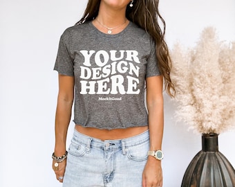 May include: A charcoal gray crop top with the text "YOUR DESIGN HERE" in white, with "MockitGood" below. The shirt has a raw hem and is paired with light blue denim jeans.