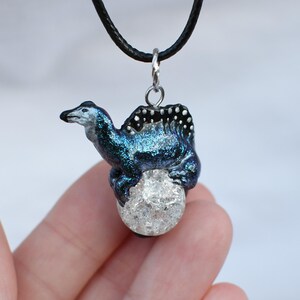 May include: A blue and black iridescent dragon pendant with a clear crystal orb, hanging from a black cord.
