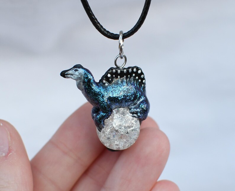May include: A blue and black iridescent dragon pendant with a clear crystal orb, hanging from a black cord.