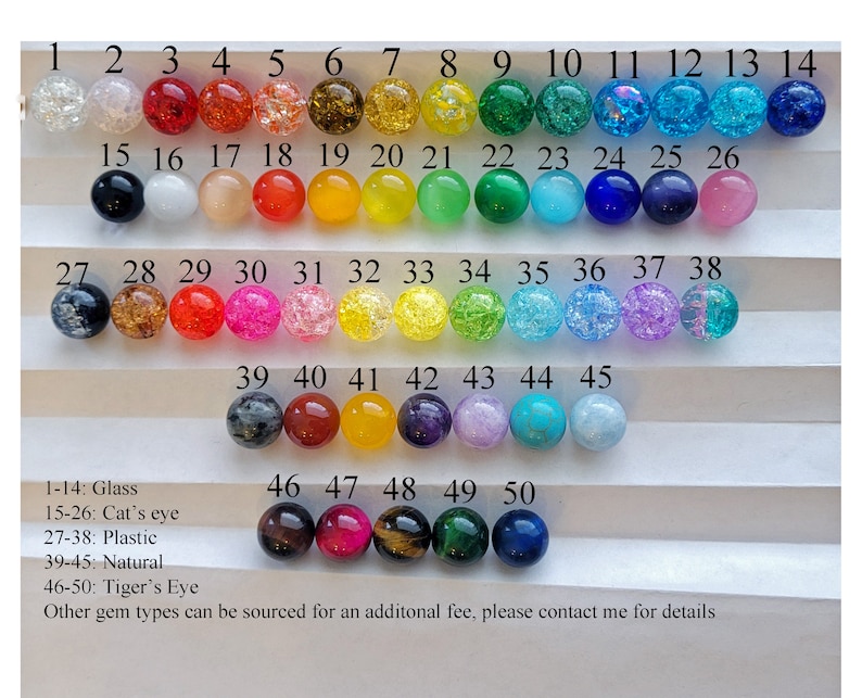 May include: A collection of 50 colorful gemstone beads, arranged in rows. The beads vary in color, including clear, red, orange, yellow, green, blue, and purple. The image includes text identifying the material of each set of beads, such as glass, cat's eye, plastic, natural, and tiger's eye.