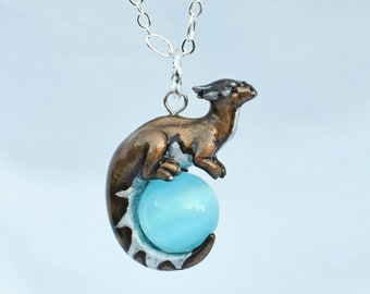 May include: A silver chain necklace with a bronze dragon pendant holding a light blue gemstone. The dragon is curled around the gemstone, with its tail wrapped around the bottom.