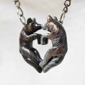 May include: A silver and bronze necklace featuring two wolf figures forming a heart shape.