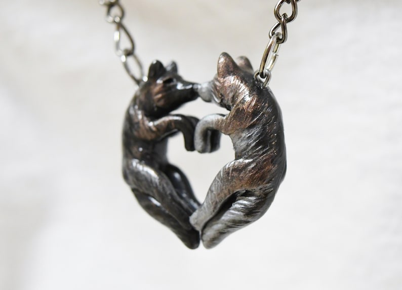 May include: A silver and bronze necklace featuring two wolf figures forming a heart shape.