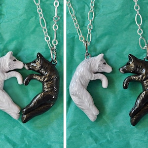 May include: Two silver necklaces with wolf pendants. The wolves are facing each other and are in a heart shape. One wolf is white and the other is black.