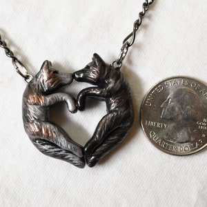 May include: A silver and black necklace featuring two wolves forming a heart shape. The necklace is about the size of a US quarter.
