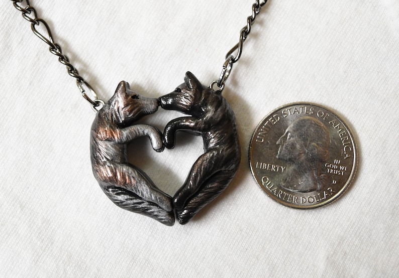 May include: A silver and black necklace featuring two wolves forming a heart shape. The necklace is about the size of a US quarter.
