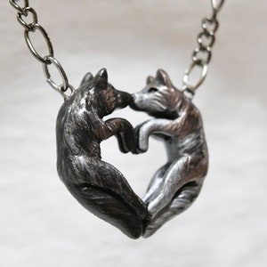 May include: A silver necklace with a pendant of two wolves facing each other, forming a heart shape.