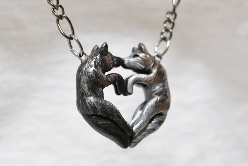 May include: A silver necklace with a pendant of two wolves facing each other, forming a heart shape.