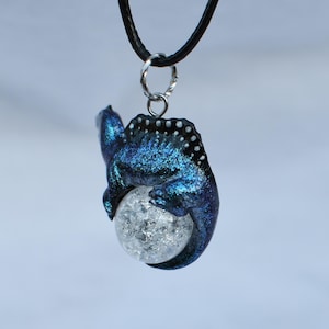 May include: A blue and black iridescent dragon pendant with a clear crystal ball. The dragon is curled around the ball, with its tail wrapped around the bottom.