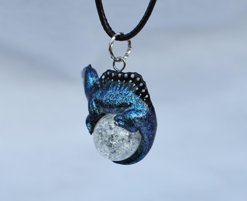 May include: A blue and black iridescent dragon pendant with a clear crystal ball. The dragon is curled around the ball, with its tail wrapped around the bottom.