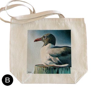May include: A canvas tote bag featuring a detailed illustration of a seagull perched on a wooden post. The bird has a black head, white body, and a red beak. The background is a soft blue, and the bag has cream-colored handles.