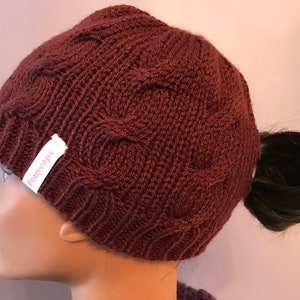 May include: A brown knitted beanie with a ponytail hole and a "Ponycaps" label. The beanie has a cable knit pattern.