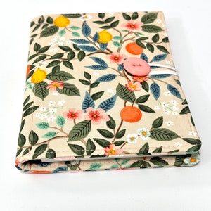 May include: A cream-colored fabric notebook cover with a floral pattern featuring lemons, oranges, and pink flowers. The cover has a pink button closure.