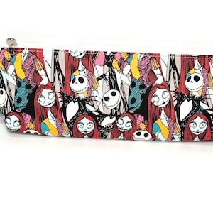 May include: A rectangular pencil case with a white zipper and a colorful pattern featuring characters from "The Nightmare Before Christmas." The design includes Sally, Jack Skellington, and other characters in a repeating pattern.