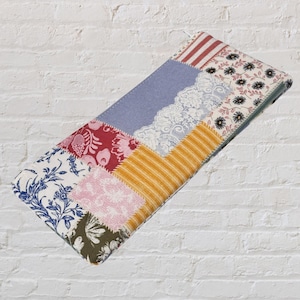 May include: A rectangular patchwork fabric item with a variety of patterned fabrics in red, blue, pink, yellow, and white. The item has a green border and is likely a case or cover.