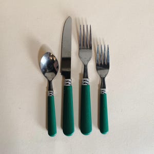 May include: A four-piece flatware set with stainless steel utensils and green handles. The set includes a spoon, a knife, and two forks. The handles are a solid, glossy green, and the set is arranged on a neutral background.