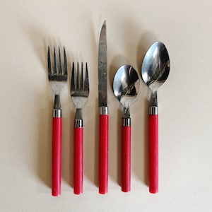 May include: Set of five silver-toned flatware with red handles. The set includes a knife, two forks, and two spoons.