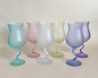 May include: Six frosted glass goblets in pastel colors: light blue, pink, white, yellow, purple, and blue. Each goblet has a unique, twisted stem and a tulip-shaped bowl. The glasses are arranged on a neutral background.