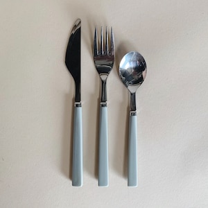 May include: A set of three silver-toned cutlery pieces with gray handles. The set includes a knife, fork, and spoon.