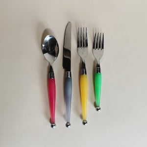 May include: A set of four pieces of flatware: a spoon, a knife, and two forks. The spoon has a red handle, the knife a gray handle, the first fork a yellow handle, and the second fork a green handle. Each handle has a silver-colored ball at the base.