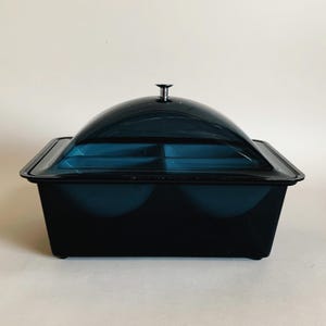 May include: A black plastic serving dish with a clear dome lid. The dish has four compartments and a silver knob on the lid.