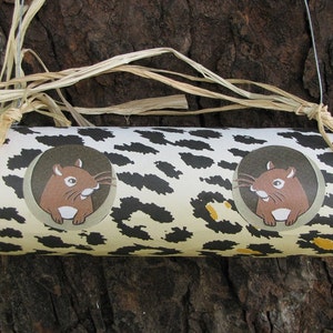 May include: A brown and white tube with a leopard print design. Two brown cartoon hamsters are printed on the tube, one on each side. The tube is hanging from a string with brown straw tied around it.