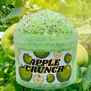 Peut inclure: Un récipient en plastique transparent rempli de slime vert avec des paillettes irisées. Le récipient porte une étiquette blanche avec le texte "APPLE CRUNCH" et un motif de pommes vertes.