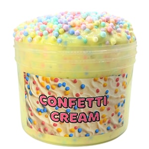 Peut inclure: Un récipient en plastique transparent rempli de slime jaune, garni de paillettes colorées. Le récipient porte une étiquette avec les mots "Confetti Cream" en lettres roses. Le slime a une texture crémeuse et est décoré de petites paillettes rondes aux couleurs pastel.