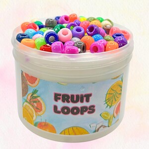 Peut inclure: Un récipient en plastique transparent rempli d'une substance blanche et de perles colorées. Le récipient porte une étiquette avec les mots "FRUIT LOOPS" et des illustrations de fruits. Les perles sont de différentes couleurs, dont le rouge, l'orange, le bleu, le vert et le violet.