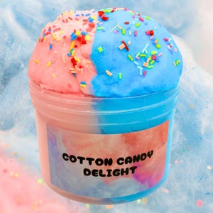 Peut inclure: Un récipient en plastique transparent rempli de slime rose et bleu à la saveur de barbe à papa. Le slime est recouvert de vermicelles colorés et le récipient porte une étiquette indiquant "Cotton Candy Delight".