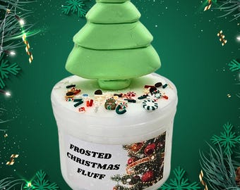 May include: A white jar of slime with a green Christmas tree topper and colorful sprinkles. The jar has a label that reads "Frosted Christmas Fluff".