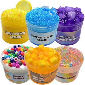 Puede incluir: Seis recipientes de plástico transparente llenos de coloridos slimes y aderezos. Los sabores incluyen "Sour Patch Lemon", "Frozen Blush Slush", "Twilight Sparkle Cubes", "Fruit Loops", "Mango Chunks" y "Rainbow Beads". Cada recipiente tiene una textura y color únicos.