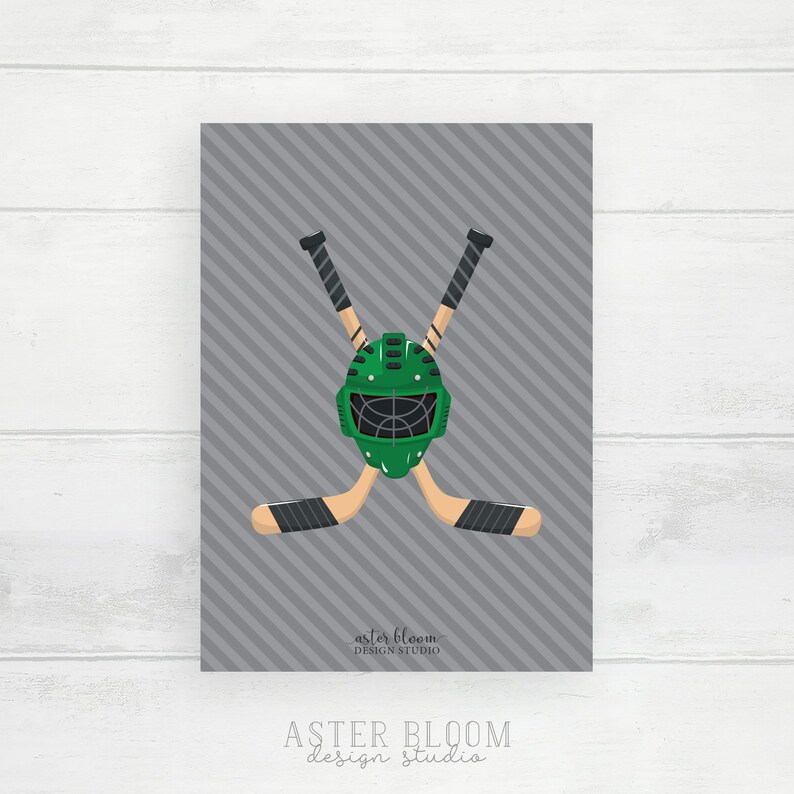 Puede incluir: M&aacute;scara de portero de hockey verde con una jaula negra, cruzada sobre dos palos de hockey negros y verdes sobre un fondo gris con rayas diagonales. El texto "aster bloom design studio" est&aacute; en la parte inferior de la imagen.