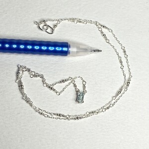 May include: A silver chain necklace with a small, rectangular, light blue gemstone pendant.