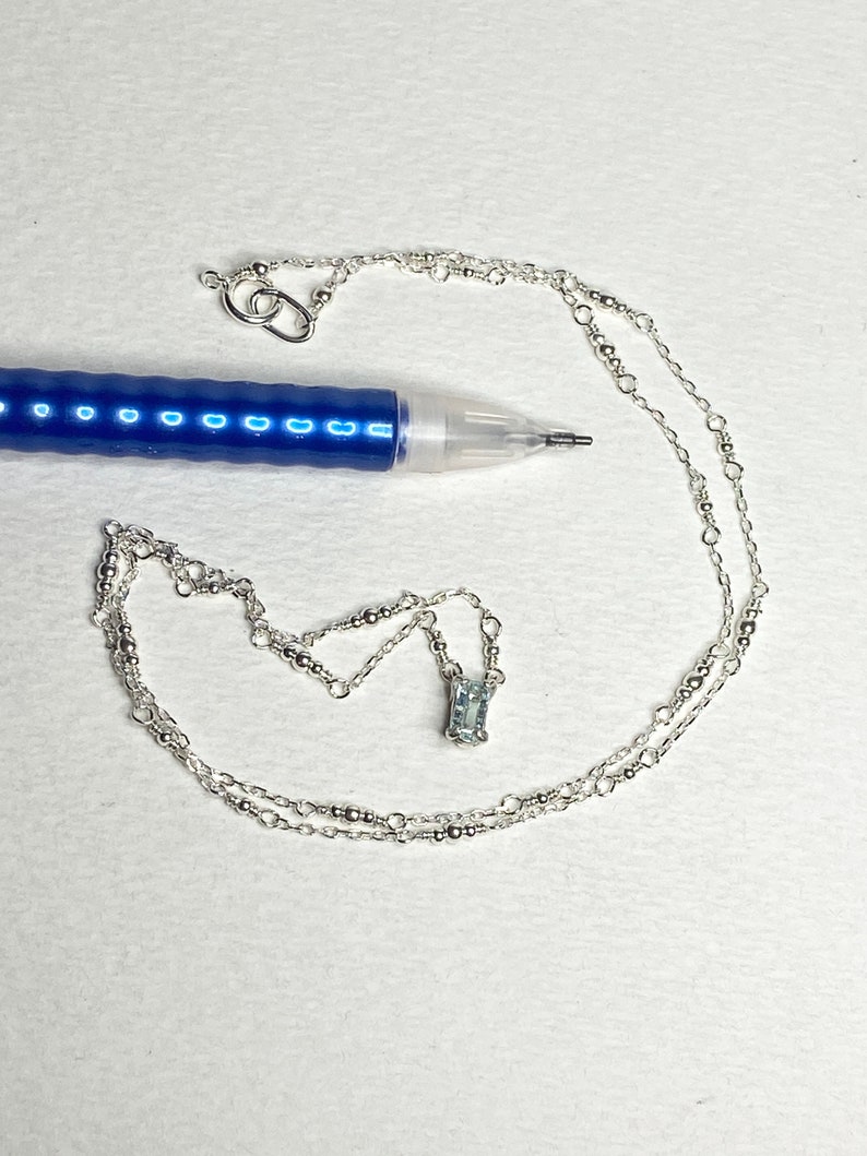 May include: A silver chain necklace with a small, rectangular, light blue gemstone pendant.