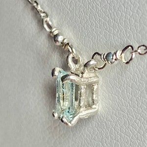 May include: A silver necklace with a light blue gemstone pendant. The pendant is set in a silver cage.