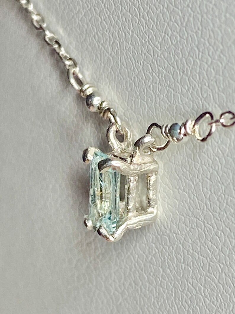 May include: A silver necklace with a light blue gemstone pendant. The pendant is set in a silver cage.