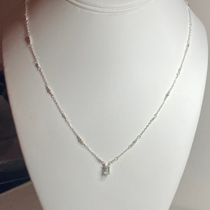 May include: A delicate silver chain necklace with a small, clear gemstone pendant.