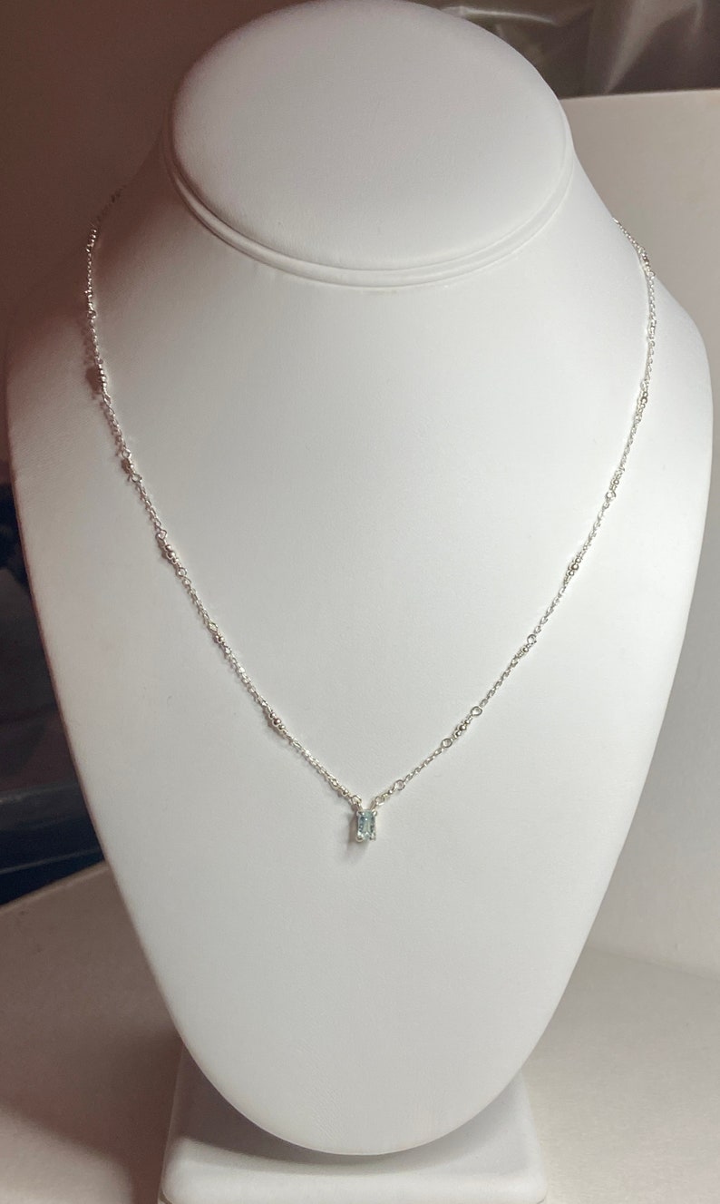 May include: A delicate silver chain necklace with a small, clear gemstone pendant.