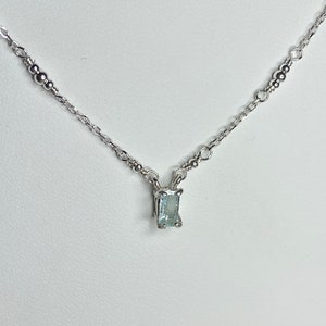 May include: A delicate silver chain necklace with a small, rectangular aquamarine gemstone pendant.