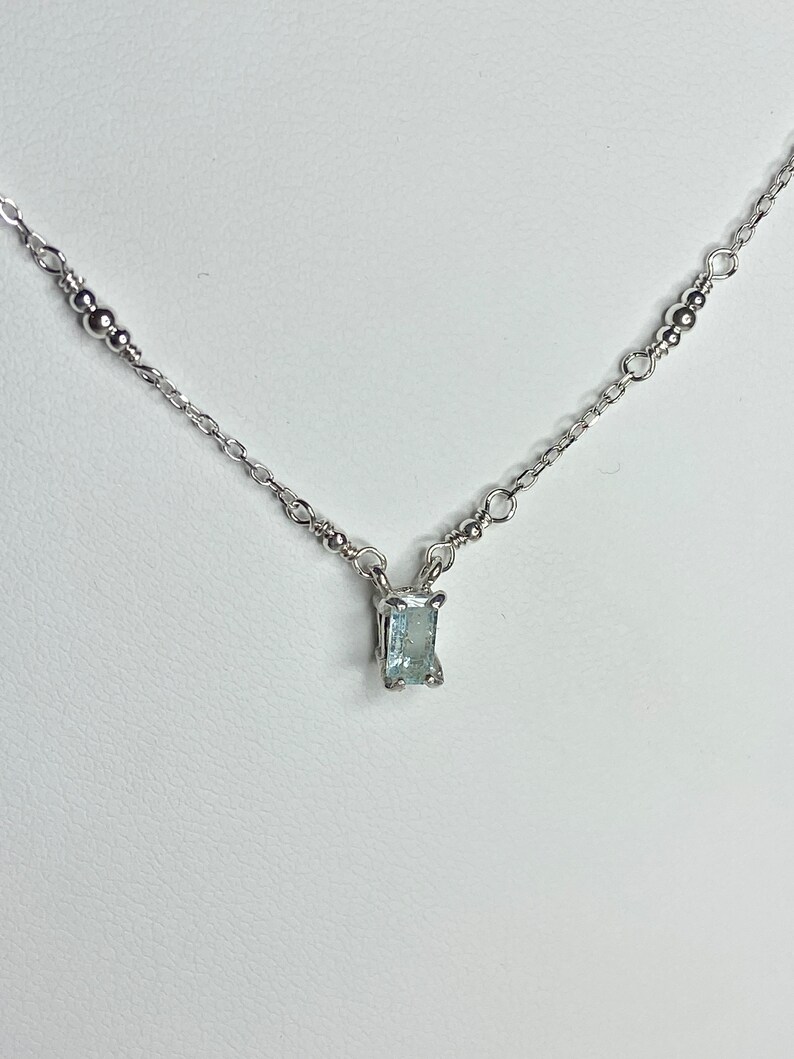 May include: A delicate silver chain necklace with a small, rectangular aquamarine gemstone pendant.
