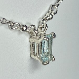 May include: A silver chain necklace with a pendant featuring a light blue aquamarine gemstone set in a silver frame.