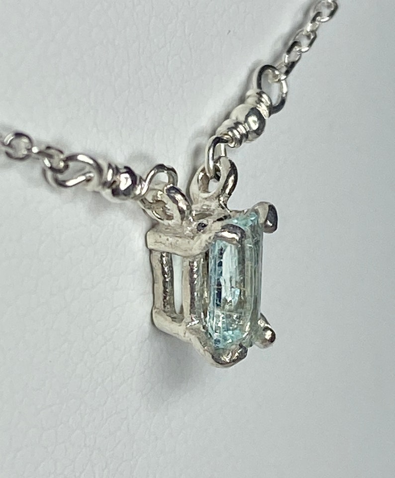 May include: A silver chain necklace with a pendant featuring a light blue aquamarine gemstone set in a silver frame.