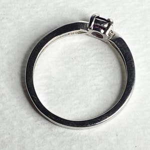 Op de afbeelding: Een zilveren ring met een enkele, kleine, donkerpaarse edelsteen in een kraalbezetting.