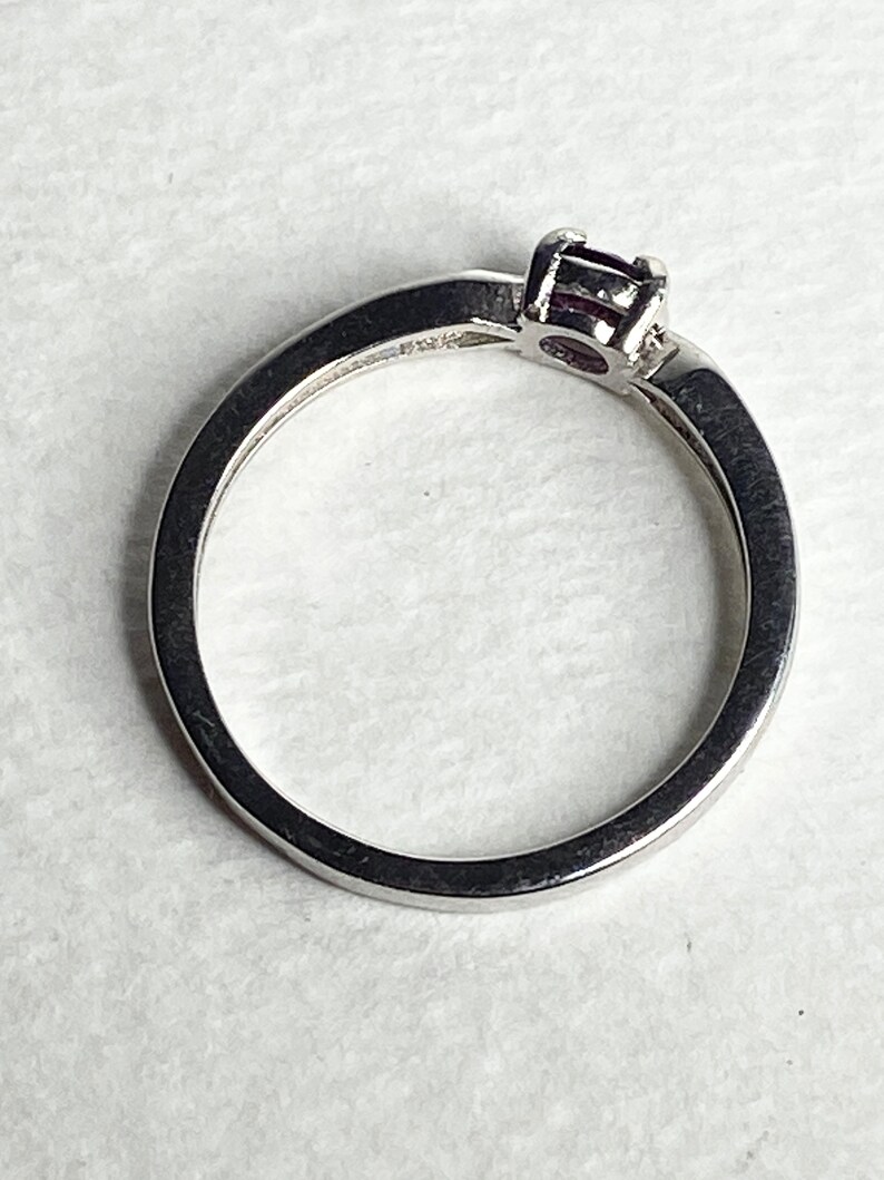 Op de afbeelding: Een zilveren ring met een enkele, kleine, donkerpaarse edelsteen in een kraalbezetting.