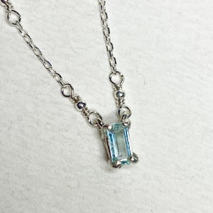 May include: A delicate silver chain necklace with a small, rectangular aquamarine gemstone pendant.