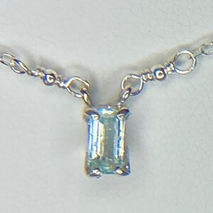 May include: A delicate silver chain necklace with a small, rectangular, light blue gemstone pendant.
